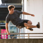 Young Adult Man Jumping Over a Fence on City Street.